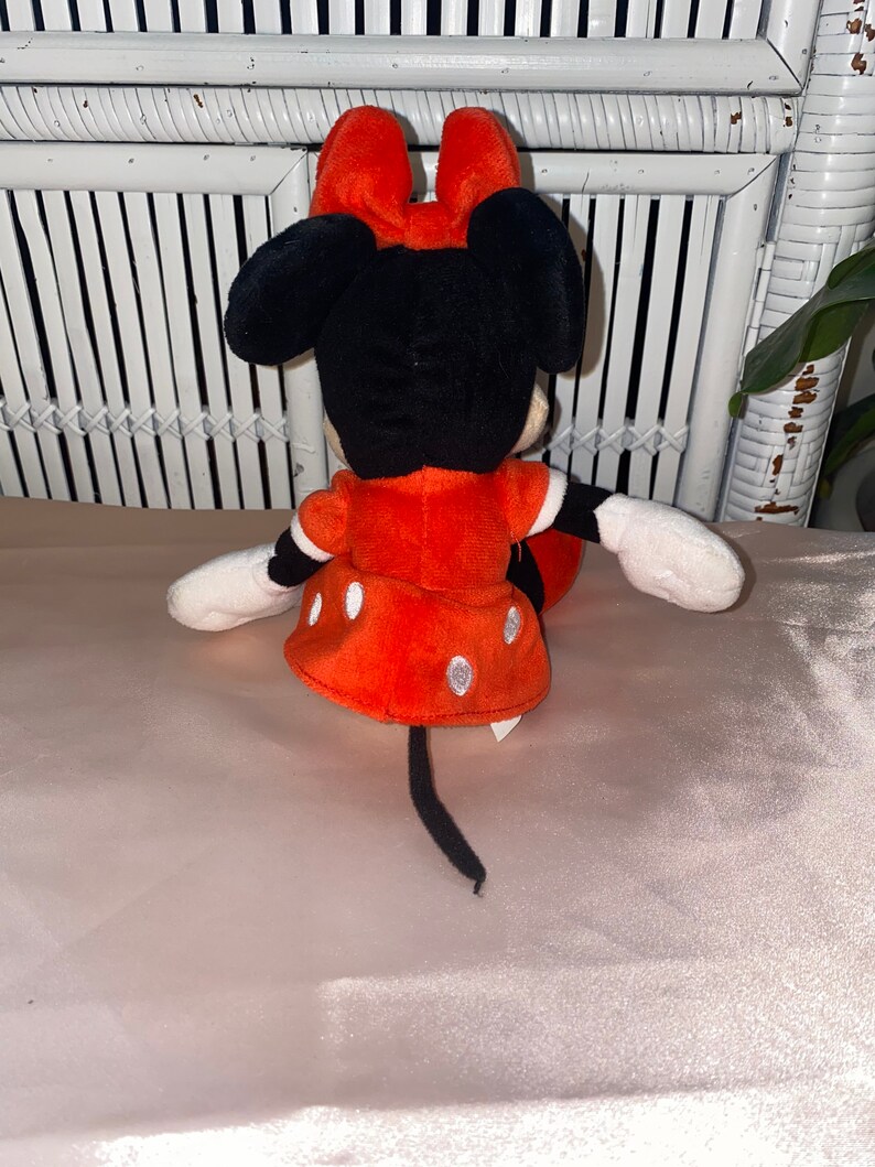 Op de afbeelding: Een rood en zwart pluche speelgoed van Minnie Mouse. Ze draagt een rode jurk met witte stippen en heeft een zwarte staart.
