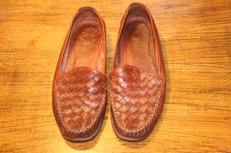 Op de afbeelding: Een paar bruine leren loafers met een geweven patroon. De loafers hebben een spitse neus en een gestikte naad rond de rand.
