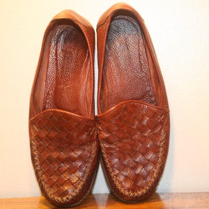 Op de afbeelding: Een paar bruine leren geweven loafers. De loafers hebben een spitse neus en een geweven leren bovenwerk.
