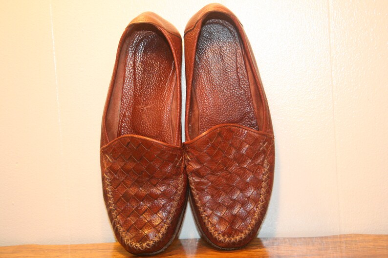Op de afbeelding: Een paar bruine leren geweven loafers. De loafers hebben een spitse neus en een geweven leren bovenwerk.