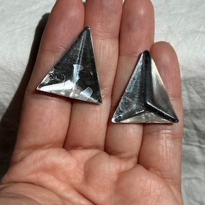 May include: A pair of silver triangle-shaped earrings. The earrings are made of a shiny metal and have a geometric design.