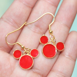 May include: A pair of gold dangle earrings with red circle charms in the shape of Mickey Mouse's head.
