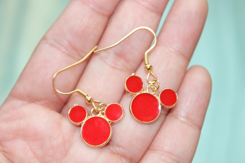 May include: A pair of gold dangle earrings with red circle charms in the shape of Mickey Mouse's head.