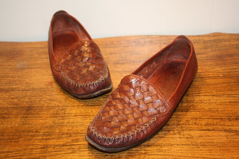 Op de afbeelding: Een paar bruine leren geweven loafers. De loafers hebben een spitse neus en een gestikte naad rond de rand.