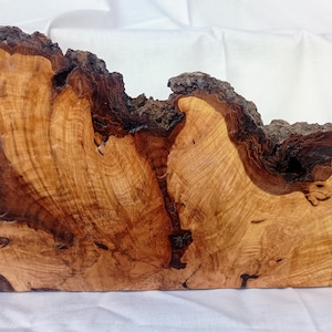 May include: A natural wood slab featuring a light tan interior with prominent swirling grain patterns and dark brown, rugged bark edges. The piece has an irregular, organic shape with a smooth, polished face and a rough, textured perimeter.