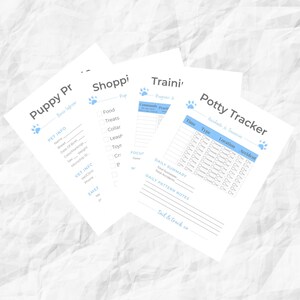 May include: A stack of four white paper sheets with blue text and paw print icons. The sheets include "Puppy Info", "Shopping", "Training", and "Potty Tracker" forms. The forms are designed to track a puppy's information and progress.