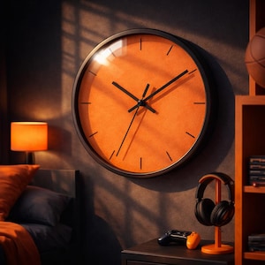 Puede incluir: Un reloj de pared grande y redondo con marco negro y esfera naranja. El reloj tiene manecillas negras y marcadores negros simples para las horas. Está montado en una pared gris oscura, con una lámpara y otra decoración visible.