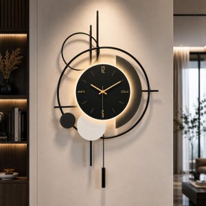 May include: A wall clock featuring a circular black face with gold hands and numerals at 12, 3, 6, and 9. The clock is framed by black metal geometric lines, circles, and a white disc, with a vertical pendulum and integrated backlighting.