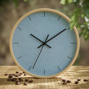 May include: A round wall clock with a light blue face and black hands and markers, set in a natural wood frame. Coffee beans are scattered on the wooden surface below the clock. The clock's diameter is approximately 30 cm.