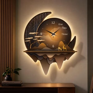 Könnte beinhalten: Eine Wanduhr in Form eines Halbmonds mit dunkelbraunem Zifferblatt, das die Zahlen 6, 9, 12 sowie die Wörter One, Two, Three zeigt. Das Design umfasst eine geschichtete Berglandschaft, einen Baum und zwei Hirschsilhouetten mit Hintergrundbeleuchtung.