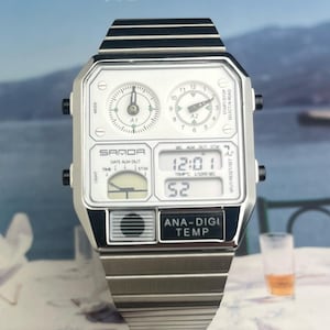 May include: A silver-toned SAMOA watch with a rectangular face and a matching metal band. The watch features two analog dials, a digital display showing the time, and the text "ANA-DIGI TEMP". The watch is set against a blurred background.