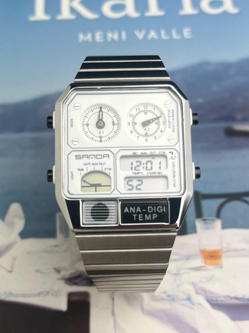 May include: A silver-toned SAMOA watch with a rectangular face and a matching metal band. The watch features two analog dials, a digital display showing the time, and the text "ANA-DIGI TEMP". The watch is set against a blurred background.