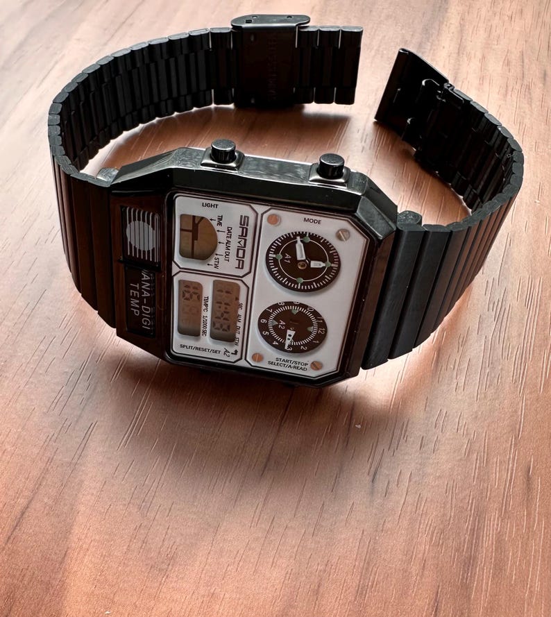 Peut inclure: Une montre-bracelet num&eacute;rique et analogique noire avec un bracelet &agrave; maillons en m&eacute;tal. Le cadran rectangulaire porte l'inscription SAMOA, ANA-DIGI TEMP et diverses &eacute;tiquettes de fonction. Elle comprend deux cadrans analogiques circulaires.