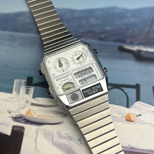 May include: A silver-toned SAMDA digital watch with an integrated analog display. The watch face is white with black numerals and hands. The watch band is made of silver metal links. The watch displays the time, date, and temperature.