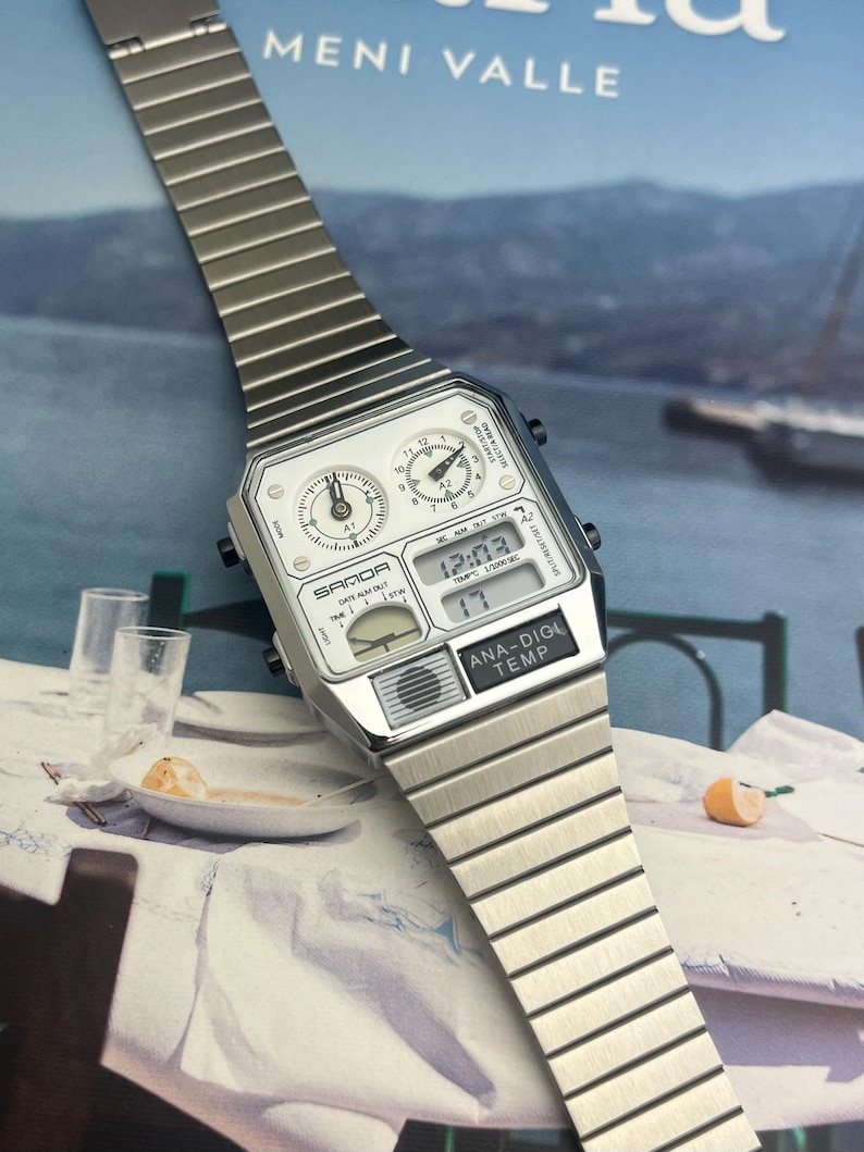 May include: A silver-toned SAMDA digital watch with an integrated analog display. The watch face is white with black numerals and hands. The watch band is made of silver metal links. The watch displays the time, date, and temperature.