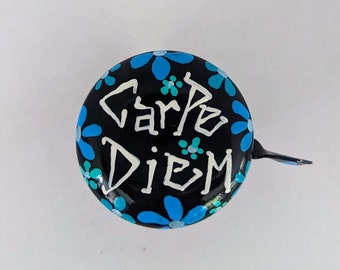 May include: Black bicycle bell with a white "Carpe Diem" inscription and blue and turquoise flower designs.