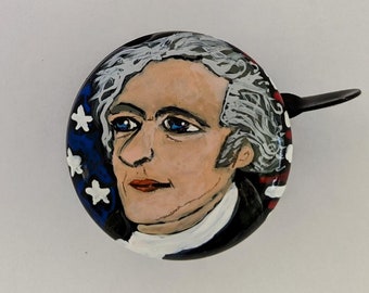 May include: A painted bicycle bell with a portrait of a man with white hair and a blue, white, and red background.