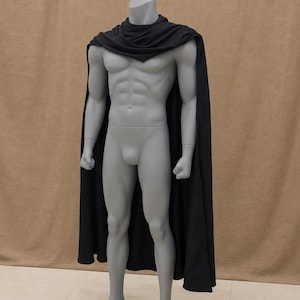 May include: A solid black cape featuring a draped cowl neckline that rests over the shoulders. The garment is constructed from a smooth, opaque fabric and extends downward to cover the back and sides of a grey, muscular, full-body mannequin.