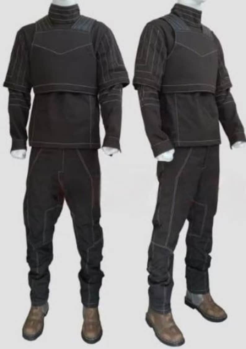 Pu&ograve; includere: Due completi tattici neri esposti su manichini. Ogni completo include un top a collo alto con protezione per il petto, maniche lunghe e pantaloni abbinati. Le cuciture bianche accentuano le cuciture. I completi sono abbinati a stivali marroni.