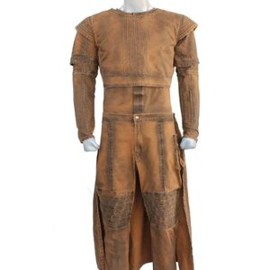 May include: A two-piece costume in shades of brown, displayed on a mannequin. The top has long sleeves and a structured design, while the pants feature a split front and knee patches. The outfit has a distressed, textured appearance.