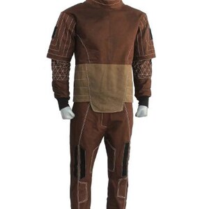 May include: Brown jumpsuit with a high collar and tan accents. The suit features white stitching details, black cuffs, and knee patches. The sleeves have a unique design with geometric patterns.