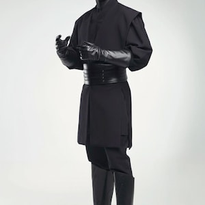 May include: A person in a black costume with a red and black face, featuring a long-sleeved tunic, trousers, gloves, and knee-high boots. The costume includes a wide belt and horns on the head. The background is plain white.
