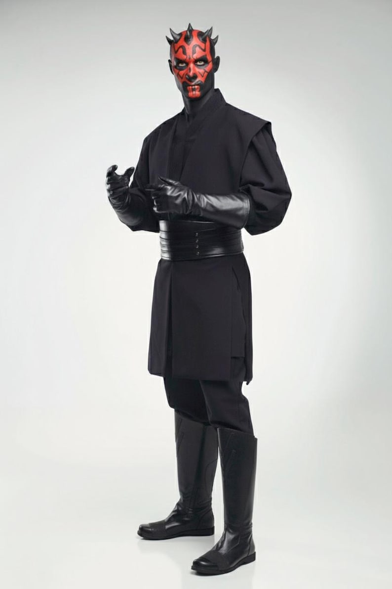 May include: A person in a black costume with a red and black face, featuring a long-sleeved tunic, trousers, gloves, and knee-high boots. The costume includes a wide belt and horns on the head. The background is plain white.