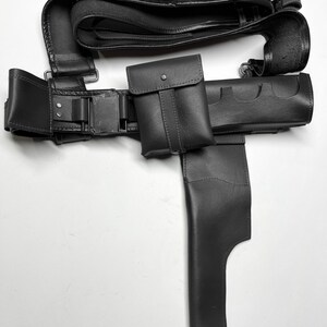 Pu&ograve; includere: Una cintura tattica in pelle nera con pi&ugrave; tasche, una fondina e porta cartucce. La cintura presenta una chiusura con fibbia ed &egrave; progettata per trasportare vari oggetti. La pelle sembra liscia e resistente.