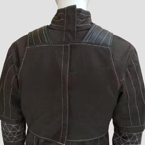 Pu&ograve; includere: Giacca nera con cuciture bianche e motivi geometrici sulle maniche. La giacca ha un colletto alto e spalle imbottite. La parte posteriore della giacca &egrave; visibile, mostrando i dettagli delle cuciture e il design.