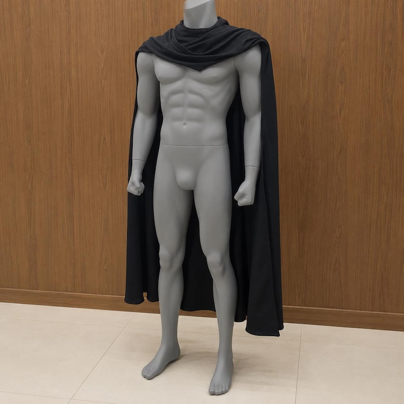 May include: A solid black cape draped over the shoulders of a grey, muscular, full-body mannequin. The cape features a simple, unadorned design that hangs straight down from the neck, covering the back and sides of the mannequin's torso and legs.