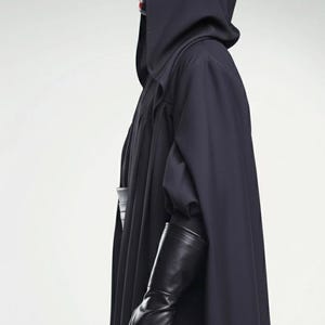 May include: A dark navy hooded cloak with long sleeves and black leather gloves. The person's face is painted red and black. The costume is likely for cosplay or a themed event.