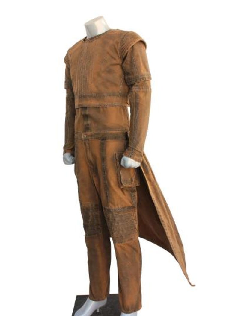 May include: A brown costume with a long coat-like back panel, long sleeves, and pants. The outfit has a textured appearance with visible stitching and a pocket on the pants. The costume is displayed on a mannequin.