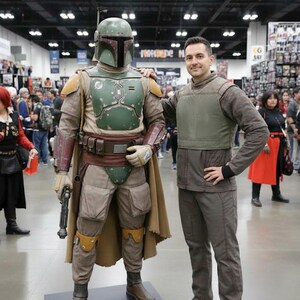 Puede incluir: Una persona posa con un disfraz de Boba Fett. El disfraz presenta un casco verde, una armadura pectoral y una capa marr&oacute;n. La persona lleva un atuendo marr&oacute;n con un chaleco verde. El escenario parece ser una convenci&oacute;n.