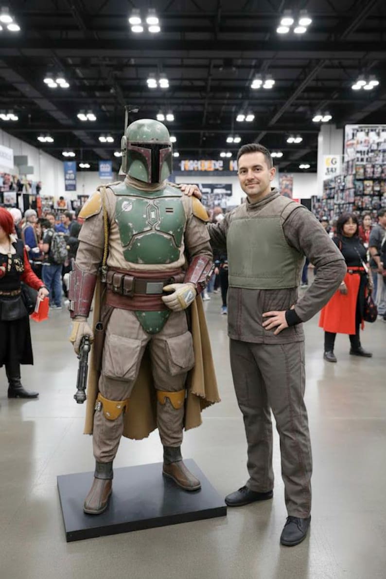 Puede incluir: Una persona posa con un disfraz de Boba Fett. El disfraz presenta un casco verde, una armadura pectoral y una capa marr&oacute;n. La persona lleva un atuendo marr&oacute;n con un chaleco verde. El escenario parece ser una convenci&oacute;n.