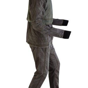Puede incluir: Un conjunto de dos piezas gris-marr&oacute;n. La chaqueta tiene un cuello alto y una textura acolchada, con una pieza de hombro verde en contraste. Las mangas tienen pu&ntilde;os negros. Los pantalones son de color y estilo a juego, con costuras visibles.