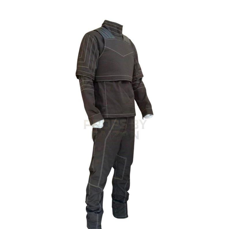 May include: A dark brown, two-piece outfit with white stitching. The outfit includes a high-collared jacket with a chest panel and long sleeves, and matching pants. The clothing is displayed on a mannequin.
