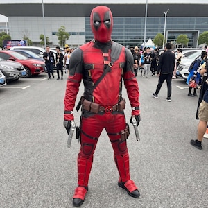 May include: A full-body Deadpool costume featuring a red and black textured suit with a matching mask, a utility belt with a central logo buckle, shoulder straps, tactical pouches on the thighs, and black boots, while holding two silver toy pistols.