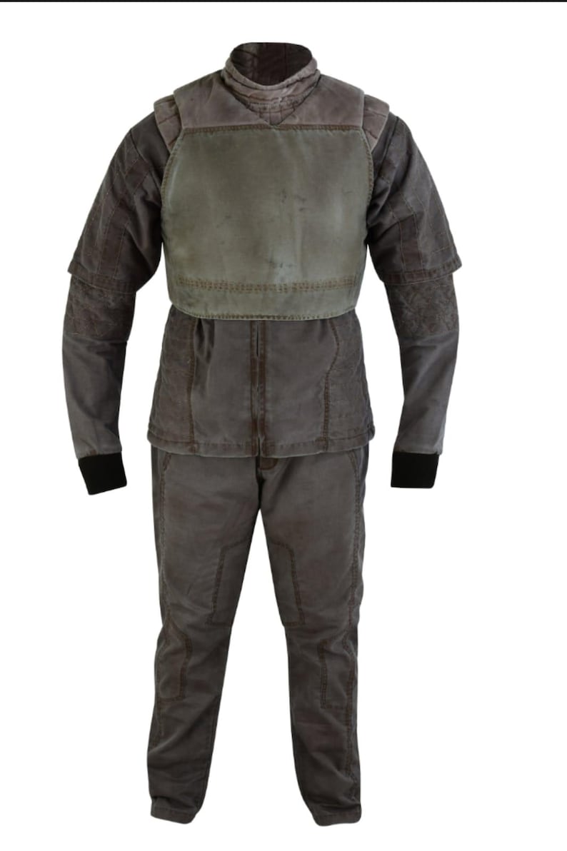 Puede incluir: Un disfraz completo de dos piezas en tonos grises y marrones. El atuendo incluye una chaqueta con peto, mangas largas y pantalones a juego. La chaqueta tiene un cuello alto y las mangas tienen pu&ntilde;os negros. Los pantalones tienen un corte entallado.