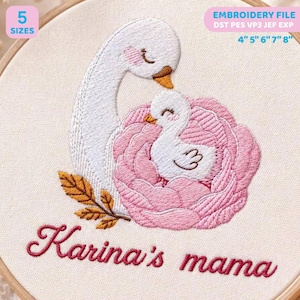 Può includere: Un ricamo su tessuto raffigurante un cigno bianco e un piccolo cigno annidati all'interno di un grande fiore rosa. Il disegno include foglie color marrone dorato e il testo "Karina's mama" in corsivo rosa. Disponibile in 10, 13, 15, 18 e 20 cm.