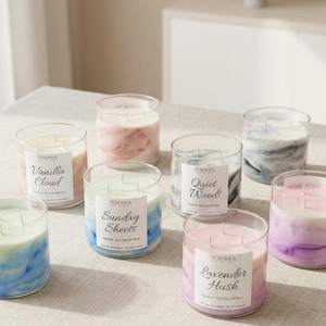 May include: A collection of glass jar candles with various colors and scents. The candles have labels with names like "Vanilla Cloud," "Sunday Sheets," and "Lavender Hush." The wax inside the jars has a marbled effect, with colors including pink, blue, and gray.