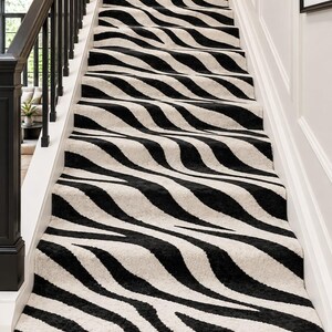 Peut inclure: Un tapis d'escalier présentant un motif zébré à fort contraste avec des rayures noires audacieuses sur un fond crème. La moquette recouvre les marches et les contremarches, s'étendant de la marche inférieure jusqu'au palier supérieur.