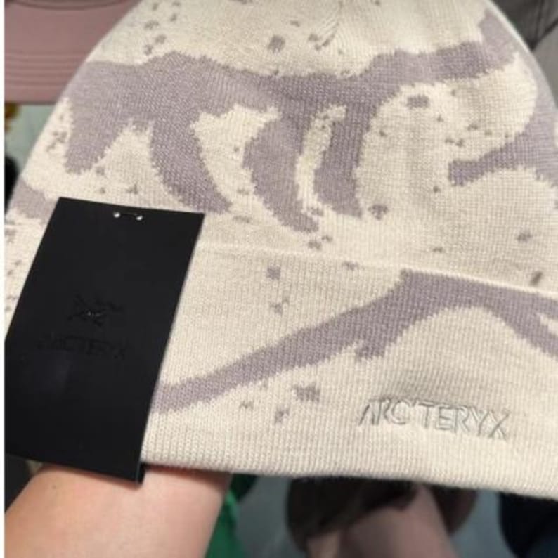 Peut inclure: Un bonnet cr&egrave;me avec un motif lavande et le nom de la marque "Arc'teryx" brod&eacute; sur le c&ocirc;t&eacute;. Une &eacute;tiquette noire avec le logo de la marque est attach&eacute;e. Le chapeau a un motif tachet&eacute;.