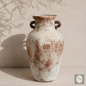 May include: A textured, off-white vase with brown accents and two dark brown handles. The vase has a wide body and a narrow neck. The overall aesthetic is rustic and aged, suggesting a vintage or antique style. The vase is likely ceramic or a similar material.