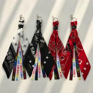 May include: Four keychains featuring fabric strips attached to silver metal rings. Each keychain includes a patterned bandana-style fabric piece and multiple narrow ribbons printed with the text MOSOHINC and colorful star icons in various patterns.