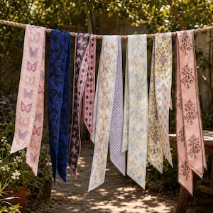 May include: A collection of eight long, narrow fabric ribbons hanging from a rope. The ribbons feature various patterns including butterflies, floral prints, geometric diamonds, and checkered designs in shades of pink, blue, yellow, and cream.