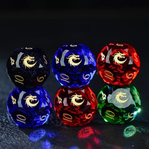 May include: Six multi-faceted polyhedral dice arranged in two stacks of three. The dice are translucent in colors of dark blue with glitter, bright blue, red, and green. Each die face features a gold dragon emblem and gold numerical markings.