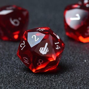 Puede incluir: Un dado de veinte caras rojo translúcido con números grabados en blanco y un gráfico blanco de una mano haciendo un gesto de dedo medio en una de sus caras triangulares. El dado está facetado y muestra los números 2, 8, 10, 12, 14 y 18.