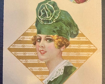 May include: A vintage postcard featuring a woman wearing a green hat with a large flower on top. She is looking to the side and smiling. The background is a gold and white diamond pattern. A small circle in the upper right corner shows a white dog with black ears and a red collar.