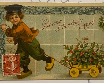 Postal francesa antigua de Bonne Année, 1910. Niño tirando de un carro lleno de acebo.