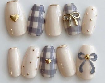 Uñas postizas de cuadros grises con detalles de corazón dorado y lazo en 3D.